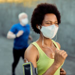 Happy black sportswoman wearing face mask while running outdoors