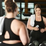 A plus-size woman in active wear works out in a gym, celebrating strength and self-love.