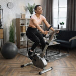 Full length portrait of young sportswoman training at home gym doing cardio on stationary bike.