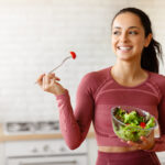 Fitness lady enjoys a healthy salad in kitchen at home