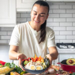 A young woman with a plate of vegetables, rice and eggs in the kitchen.
