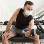 vista-frontal-de-um-homem-na-academia-com-mascara-medica-malhando