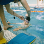 Swim coach helping kid with a cap in a pool